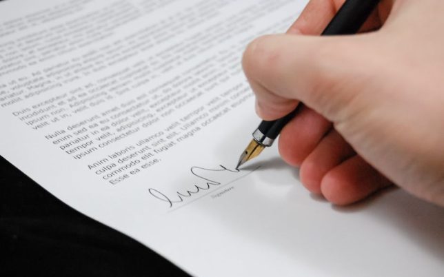 Close-up of a hand signing a legal document with a fountain pen, symbolizing signature and agreement.