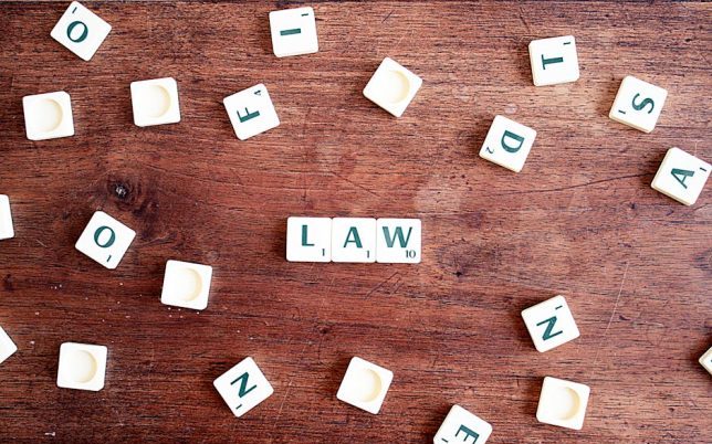 Scrabble tiles spelling 'LAW' on a wooden table, symbolizing connections to education and legality.