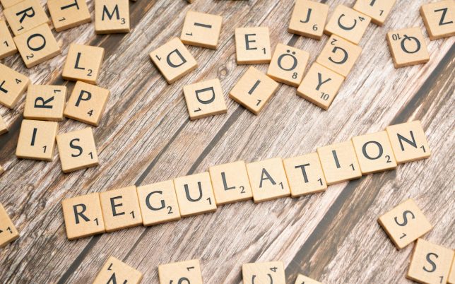 Wooden letter tiles spelling 'Regulation' on a textured wood background, conveying themes of compliance and structure.