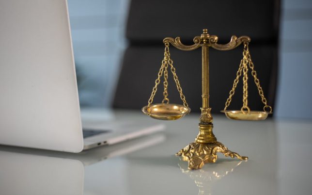 Golden justice scales on a desk beside a laptop, symbolizing law and balance.